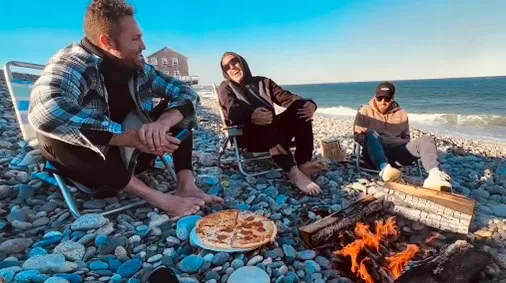 A men's group gathered around a beach campfire at golden hour